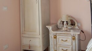 A room with a tall white wardrobe, a small white bedside table with a lamp, and a tiled floor. - La Papaya (Pisa)
