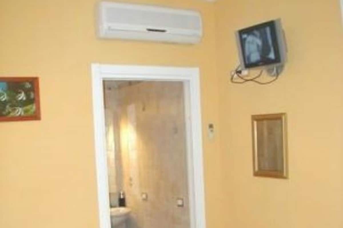 A room with two beds, a television, an air conditioning unit, a door leading to a bathroom, and a chair.