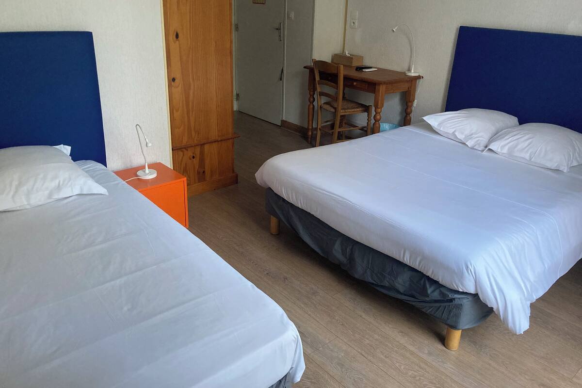 Quarto de hotel com duas camas, uma escrivaninha de madeira e um guarda-roupa.