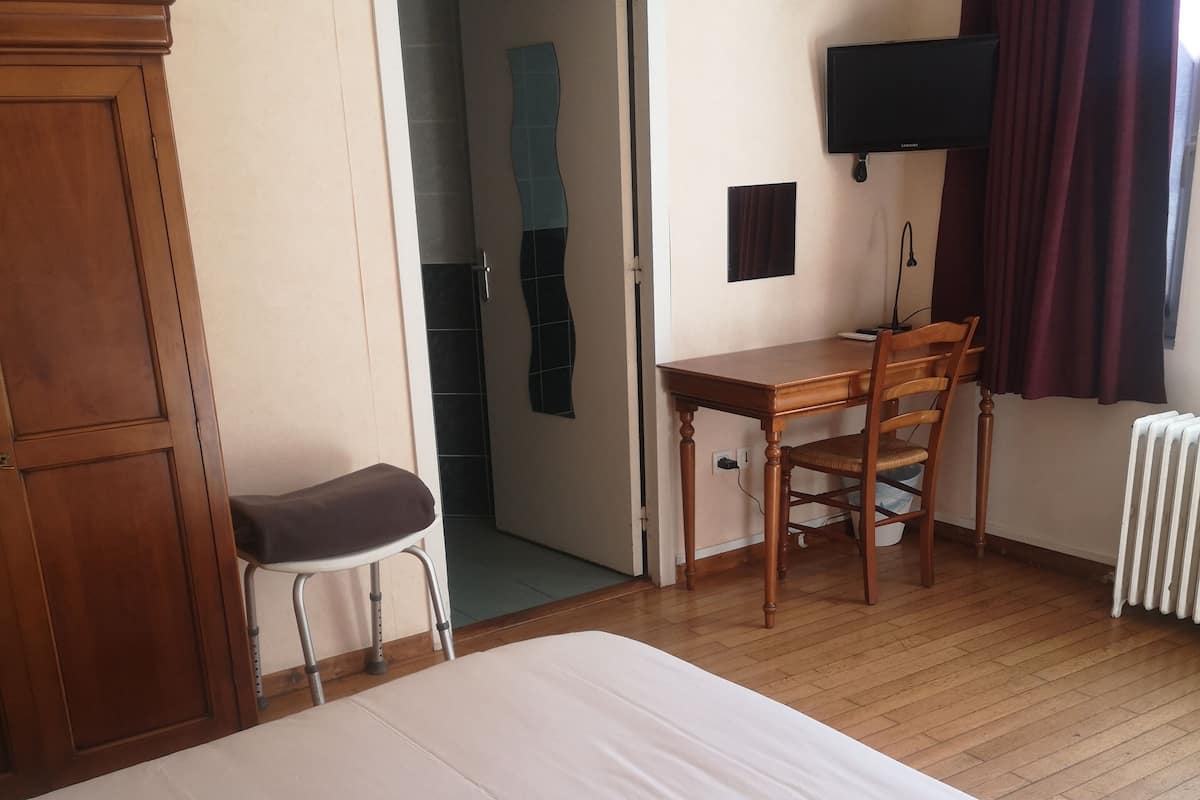 Quarto de hotel com cama, escrivaninha, cadeira, guarda-roupa, televisão e radiador.