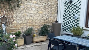 Un espace extérieur aménagé en terrasse, avec un mur en pierre, une fenêtre à treillis et des plantes en pot.