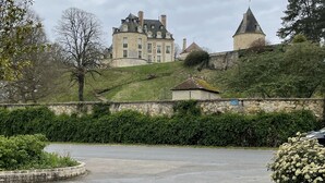 Un grand bâtiment historique doté d’une tour ronde, entouré d’une végétation luxuriante et d’une zone pavée.
