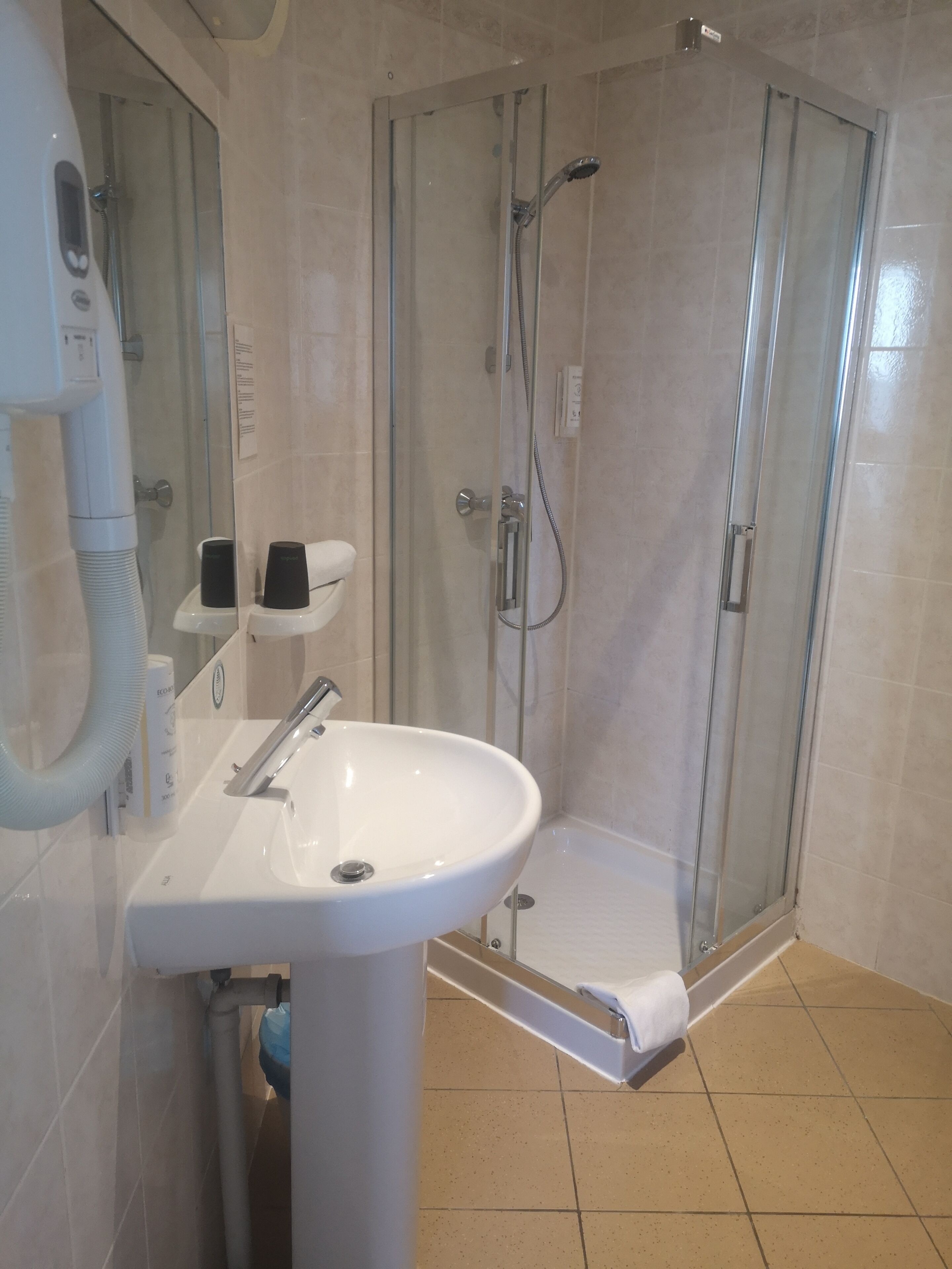 Un baño moderno con ducha de vidrio, un lavamanos blanco y un perchero.