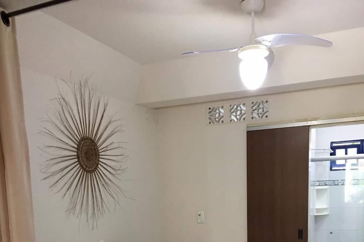 A bedroom with a bed, a ceiling fan, a decorative wall piece, and a door leading to a bathroom.