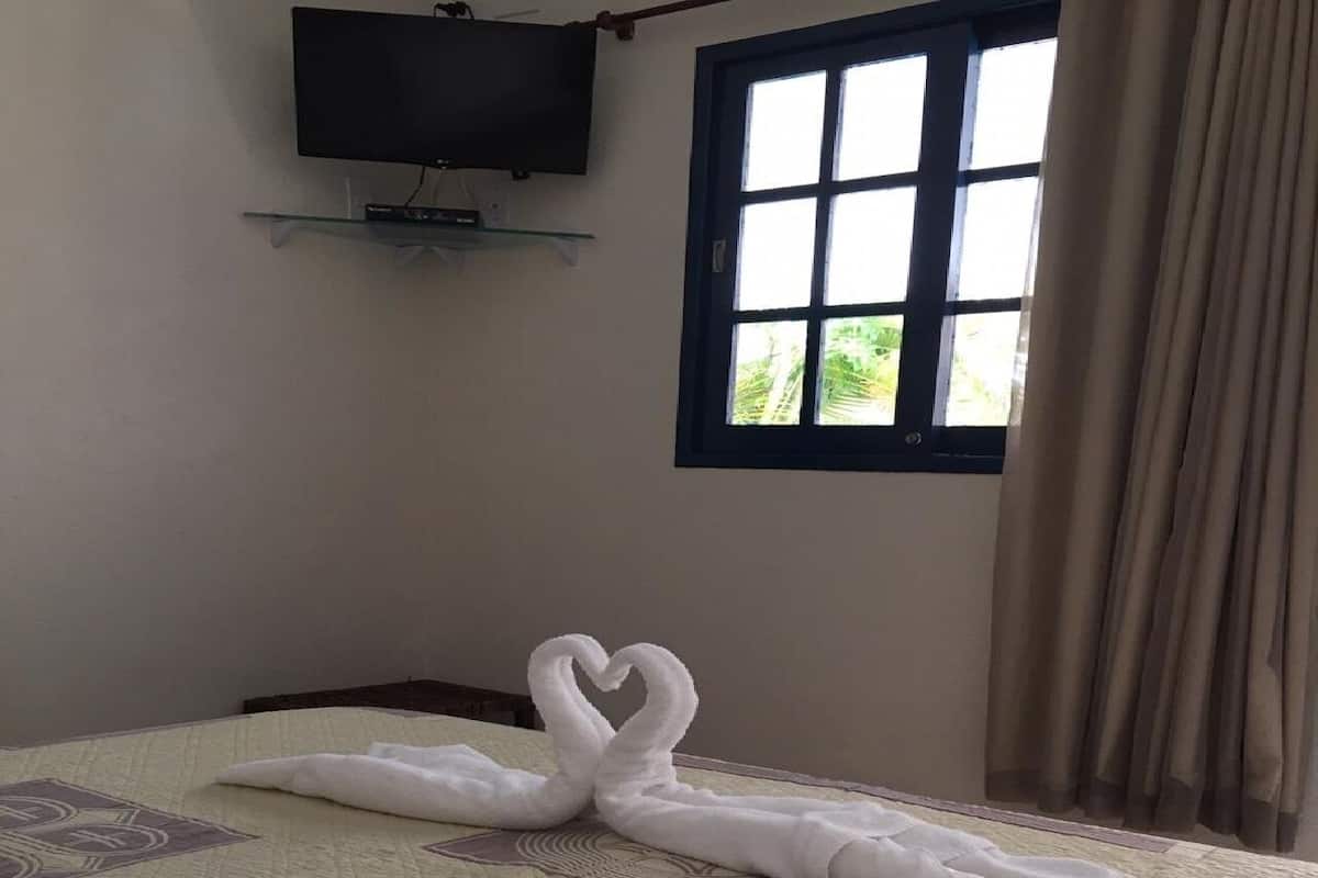 A hotel room with a bed, a TV mounted on the wall, and a window with curtains.