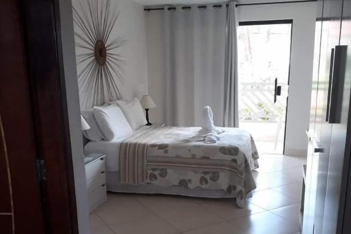 A hotel room with a bed, a nightstand, a lamp, and a view of the outdoors through a sliding door.