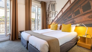 Habitación de hotel con una cama grande, cabecera de madera, mesita de noche con lámpara y vista a un edificio histórico.