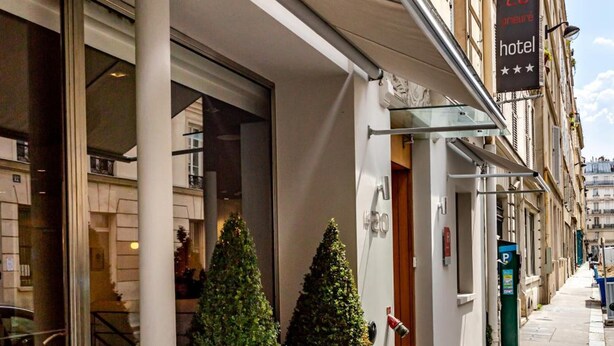 Entrada de hotel con un letrero que indica 20 habitaciones, plantas grandes en macetas y una acera despejada.