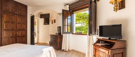 Un dormitorio con una cama grande, un armario de madera, un televisor sobre un mueble de madera y una ventana con cortinas.