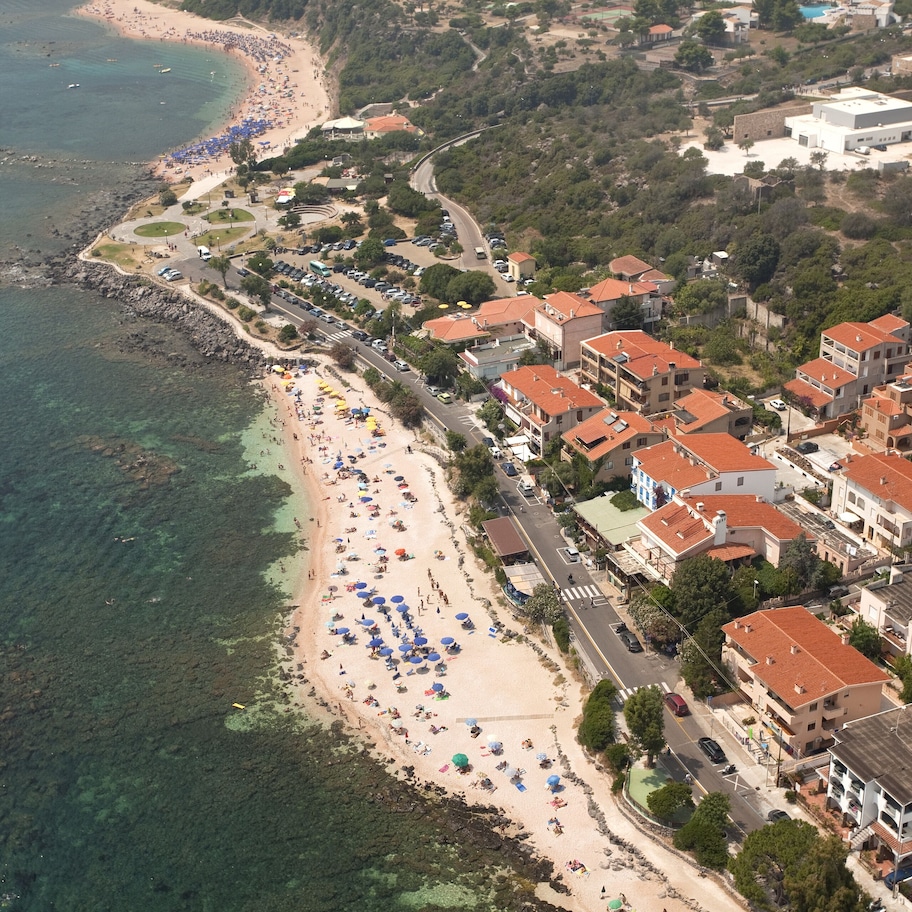 An aerial view of a coastal town with a beach, residential buildings, and clear blue waters.