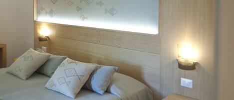 A neatly made bed with patterned pillows, a wooden headboard, and two wall-mounted nightstands with lamps.
