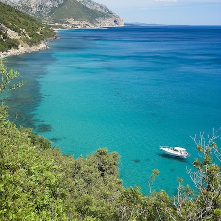 A coastal landscape with clear turquoise waters, a boat, and lush greenery.