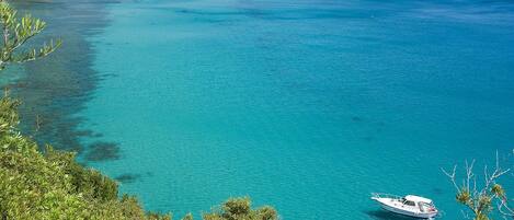 A coastal landscape with clear turquoise waters, a boat, and lush greenery.