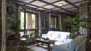A cozy living room with stone walls, a wooden ceiling, and a white sofa. There are several potted plants and a coffee table. - Hotel Costa Dorada (Dorgali)