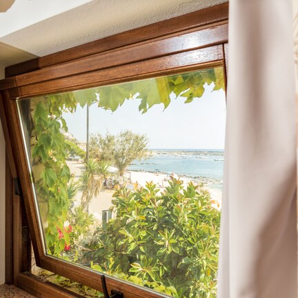 A window with a view of a beach, greenery, and a clear sky.