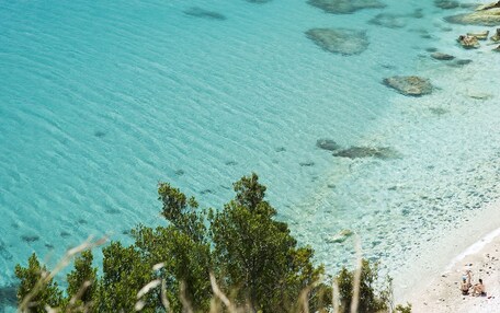 A boat on clear turquoise water near a rocky shoreline with a beach in the foreground.