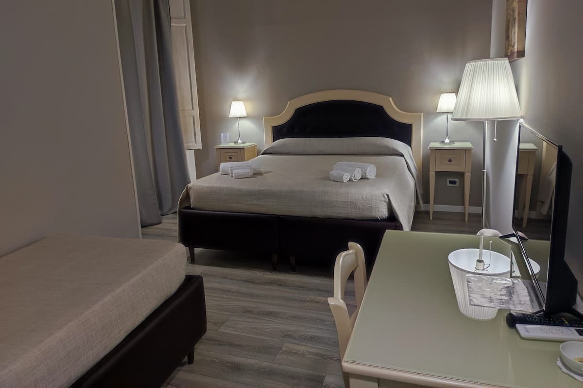 A hotel room with a bed, bedside tables, a desk, a chair, a lamp, a mirror, and a small table with a bowl and remote control.