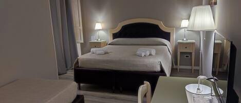 Une chambre d’hôtel comprenant un lit, des tables de chevet, un bureau, une chaise, une lampe, un miroir et une petite table avec un bol et une télécommande.