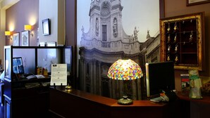 A reception desk with a colorful lamp, a computer monitor, and a framed picture of a building. - La Collegiata Guest House (Catania)