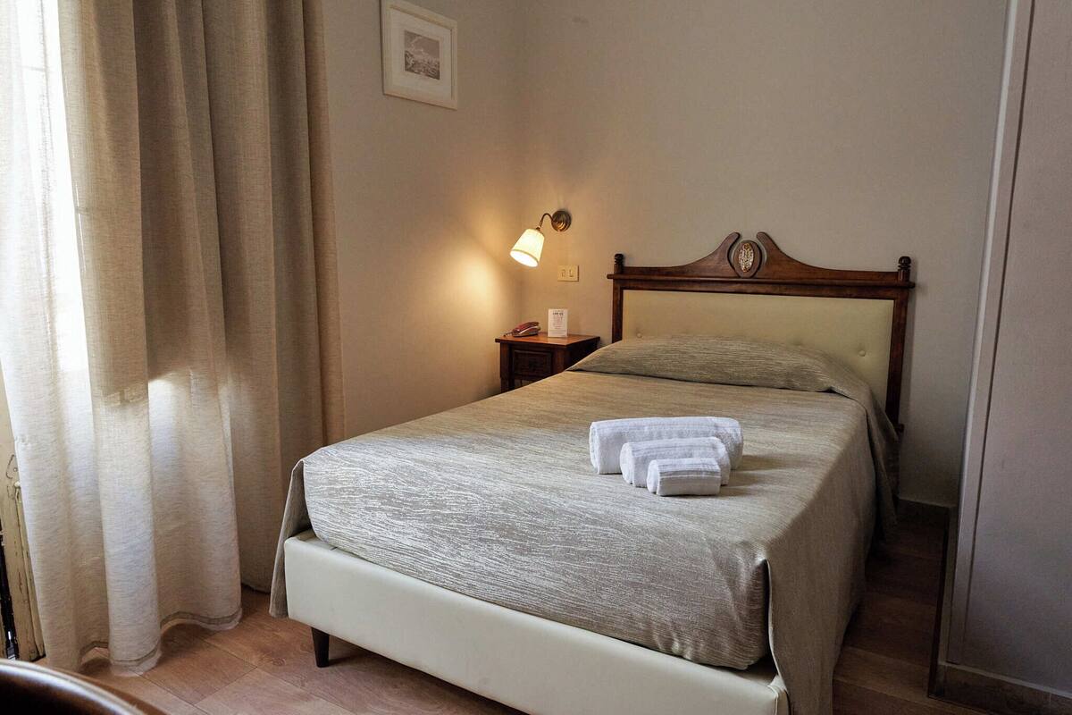 A neatly made bed with a headboard, a bedside lamp, and a nightstand with a telephone.