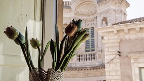 A window with a vase of flowers and a view of a historic building with ornate architecture. - La Collegiata Guest House (Catania)