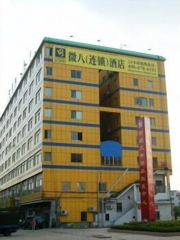A multi-story building with a yellow facade and a green roof. There is a sign with Chinese characters and a phone number.