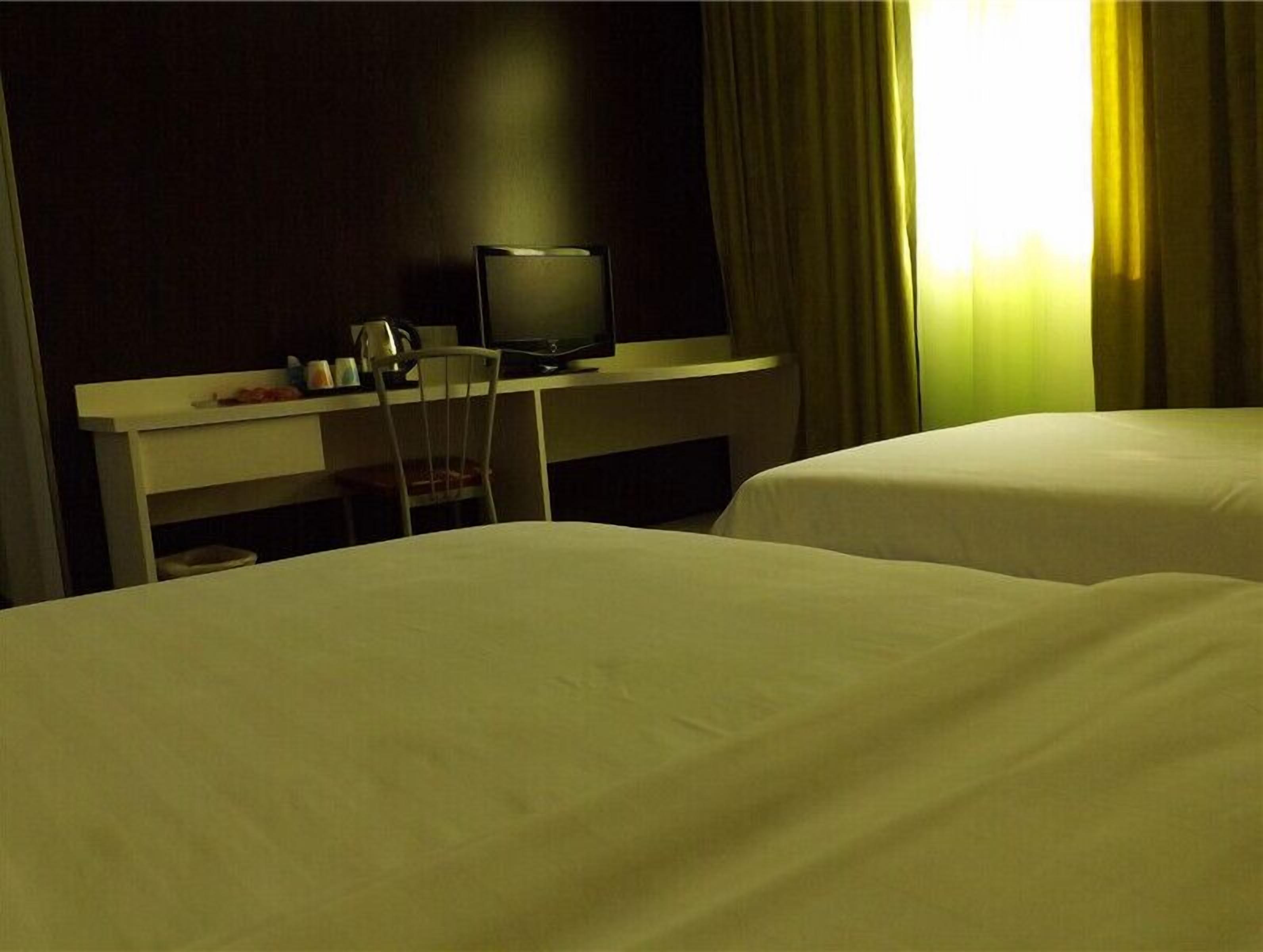 A hotel room with two beds, a desk with a television, and a chair.