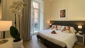 A hotel room with a large bed, a bedside table with a lamp, a potted orchid, and a view of the outside balcony. - Hotel Eletto (Sanremo)