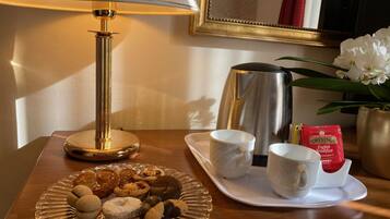 Una bandeja de desayuno con pastelería, dos tazas blancas, un hervidor de té y bolsitas de té Twinings English Breakfast sobre una mesa de madera.