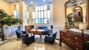 A spacious lobby with a seating area, a wooden coffee table, and a large mirror. - Hotel Eletto (Sanremo)