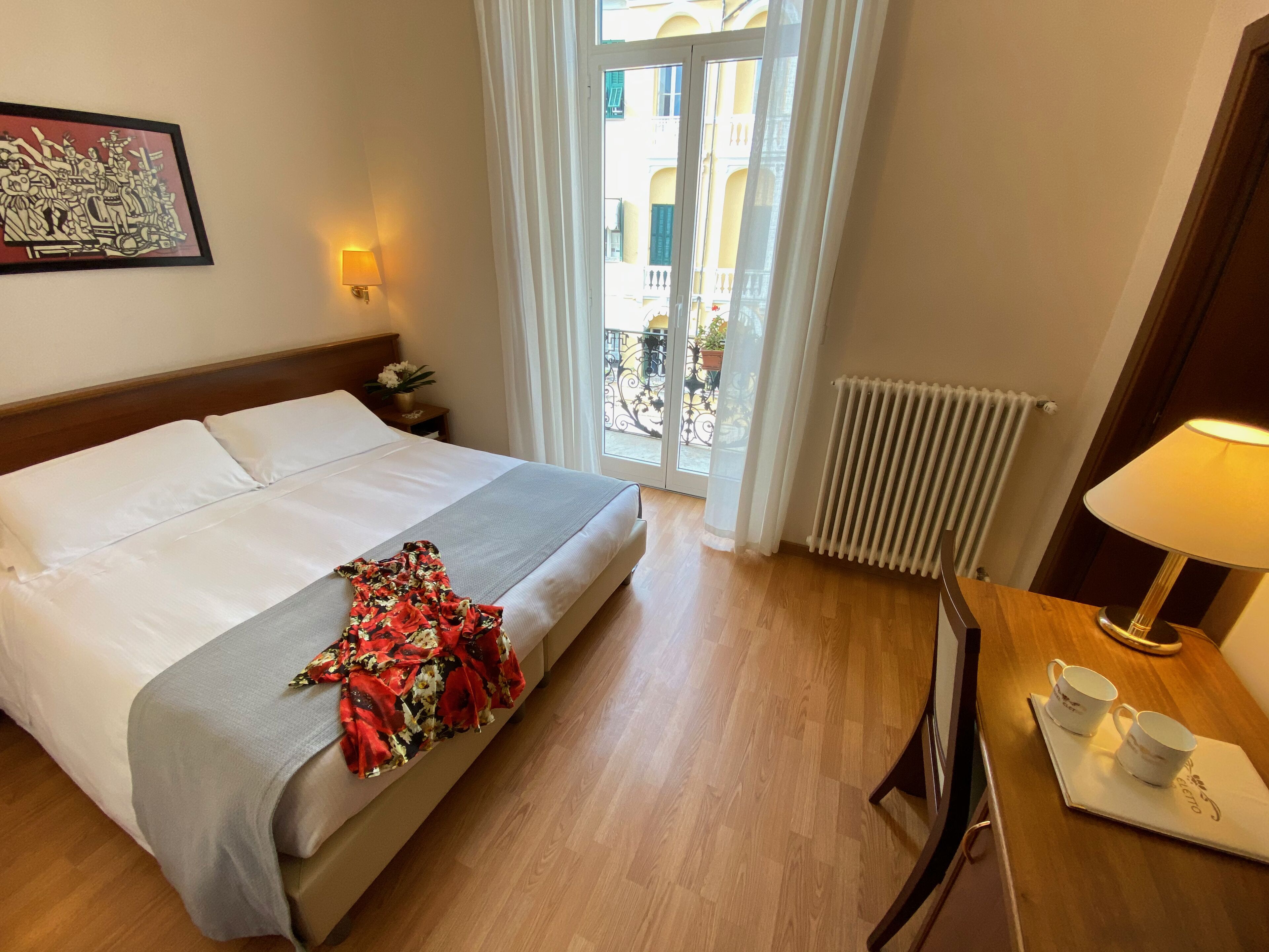 Ett hotellrum med en säng, ett skrivbord med en lampa, en stol och utsikt över balkongen.