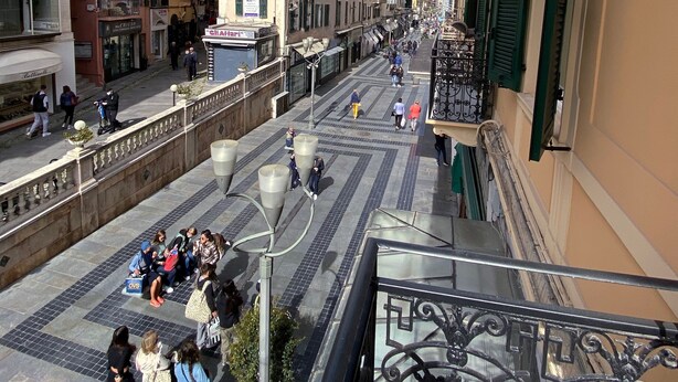 A pedestrian street with buildings on either side, a clear sky, and people walking. - Hotel Eletto (Sanremo)