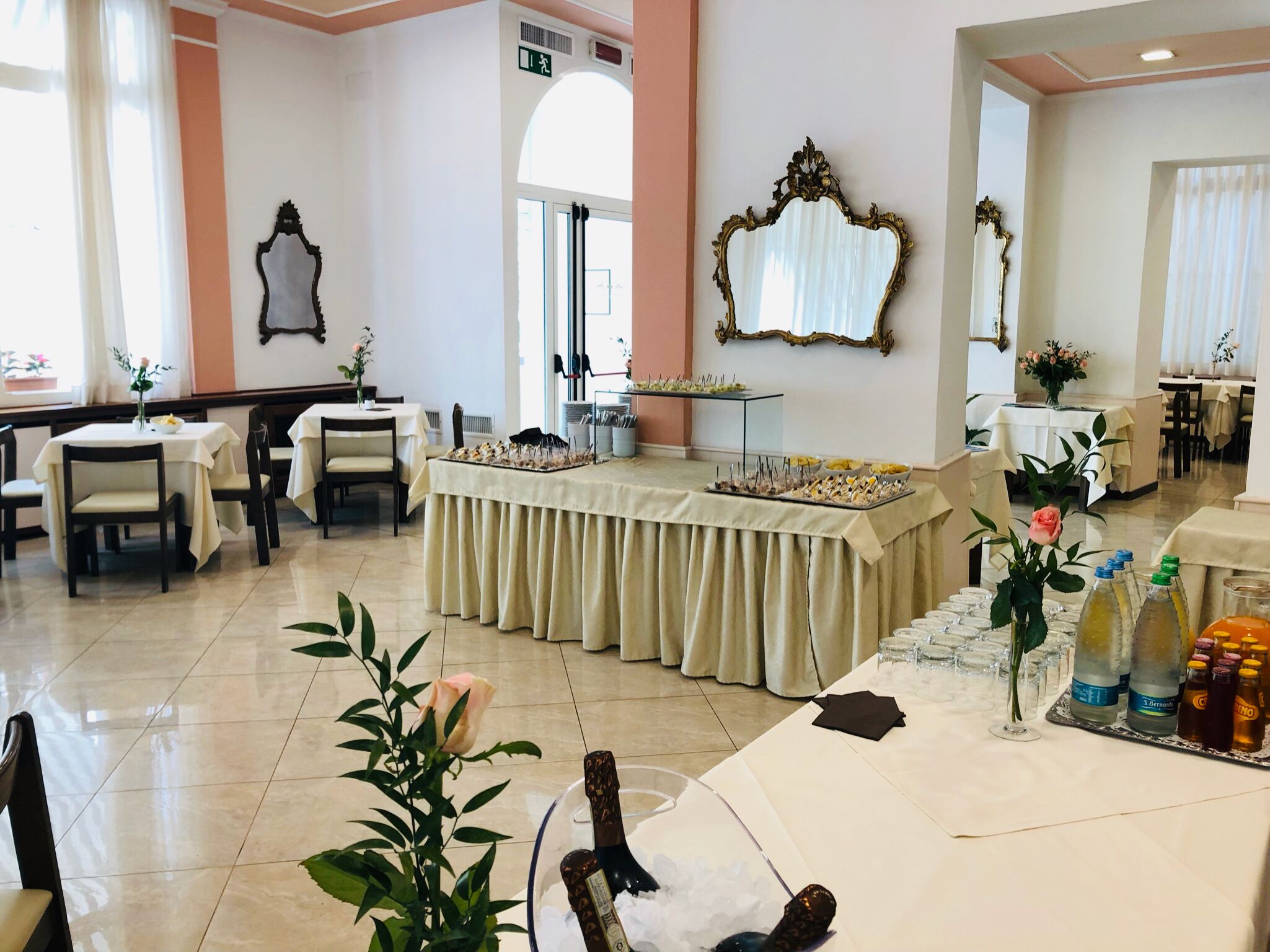 Zona pranzo di un hotel con tavoli apparecchiati per un pasto, un buffet con diversi piatti e uno specchio a parete.
