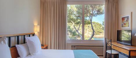 Habitación de hotel con dos camas, un escritorio con televisor y una ventana con cortinas.