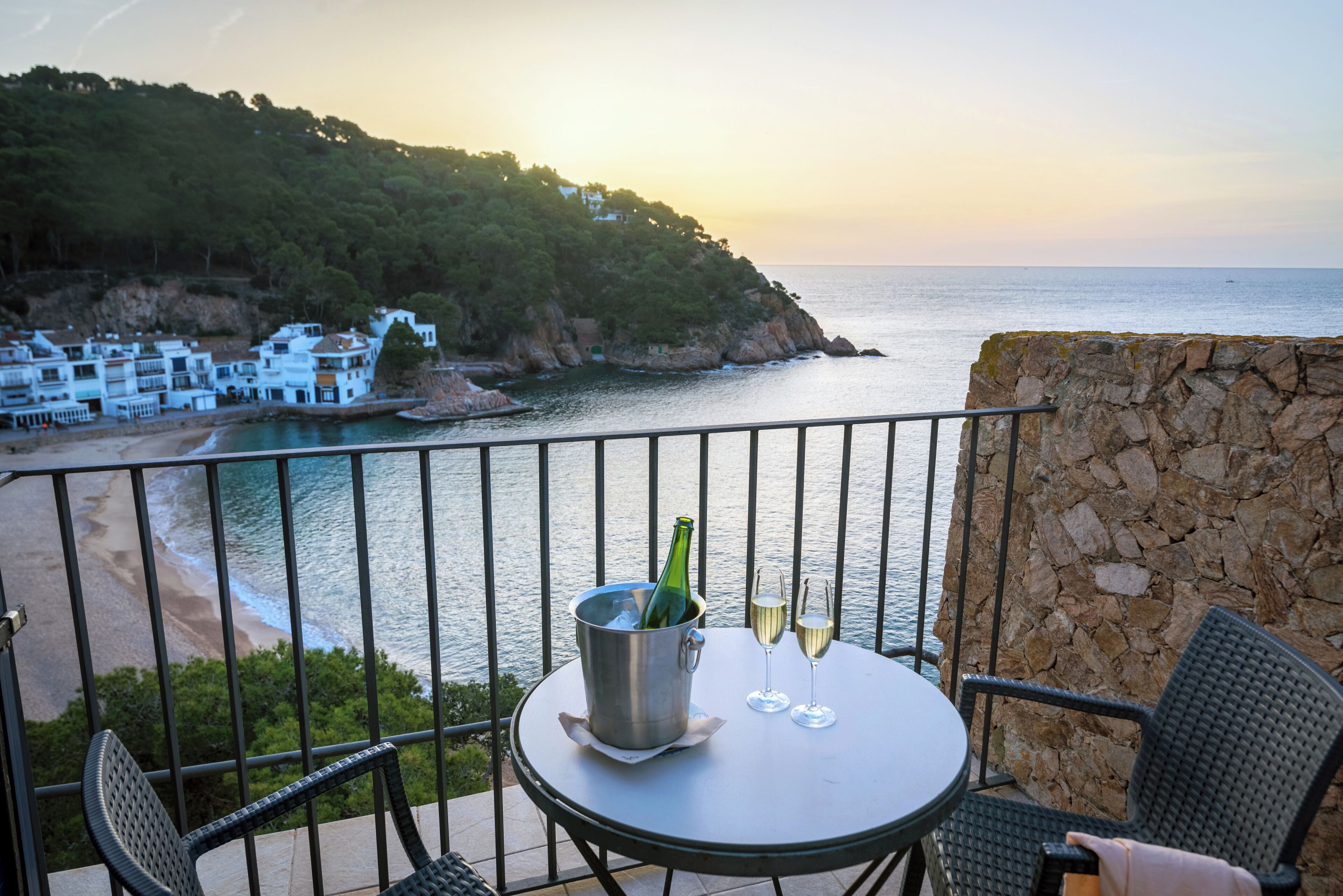 A balcony with a table, two chairs, a bottle of champagne, and two glasses.