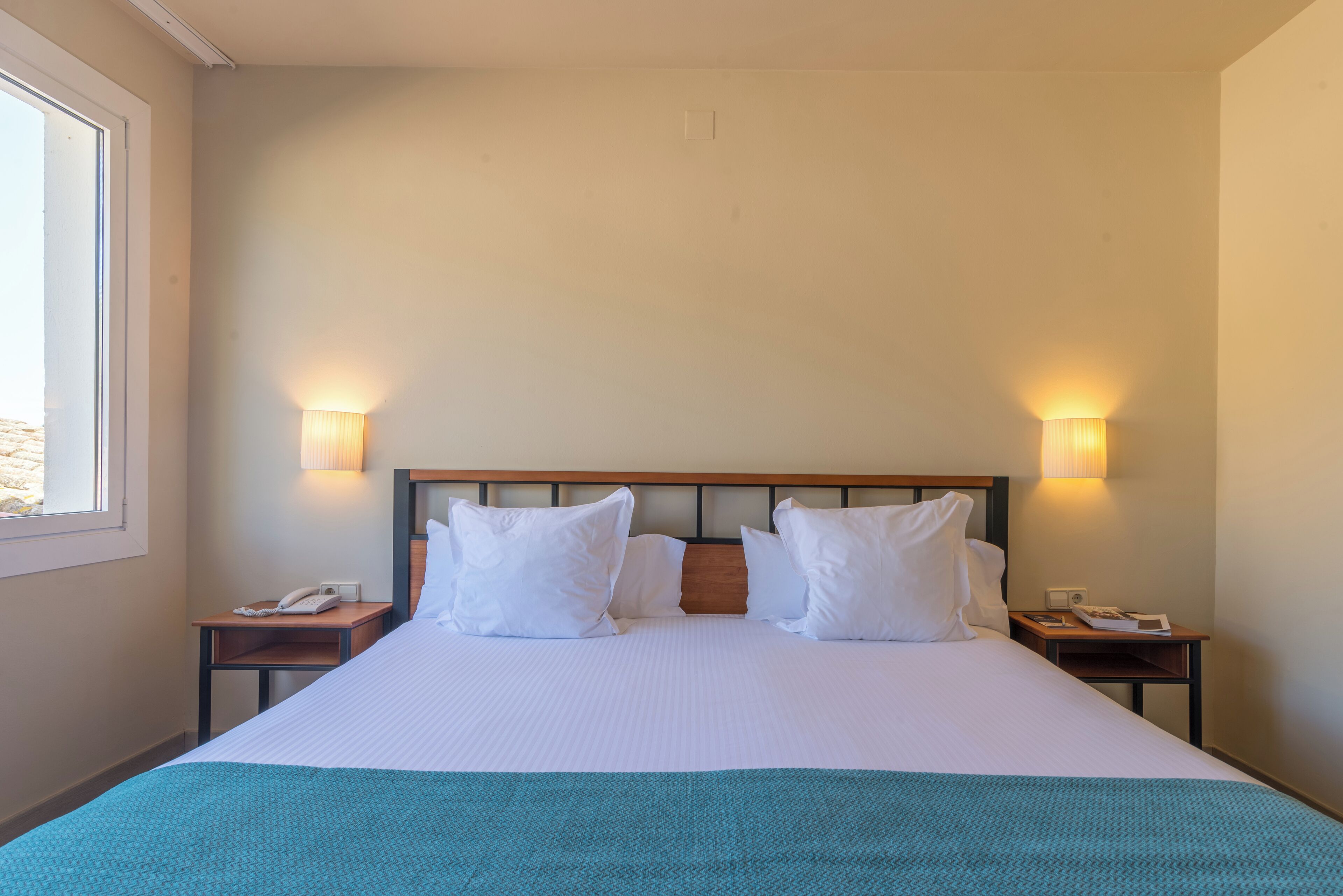 A hotel room with a large bed, two bedside tables, a nightstand, a lamp, and a window.