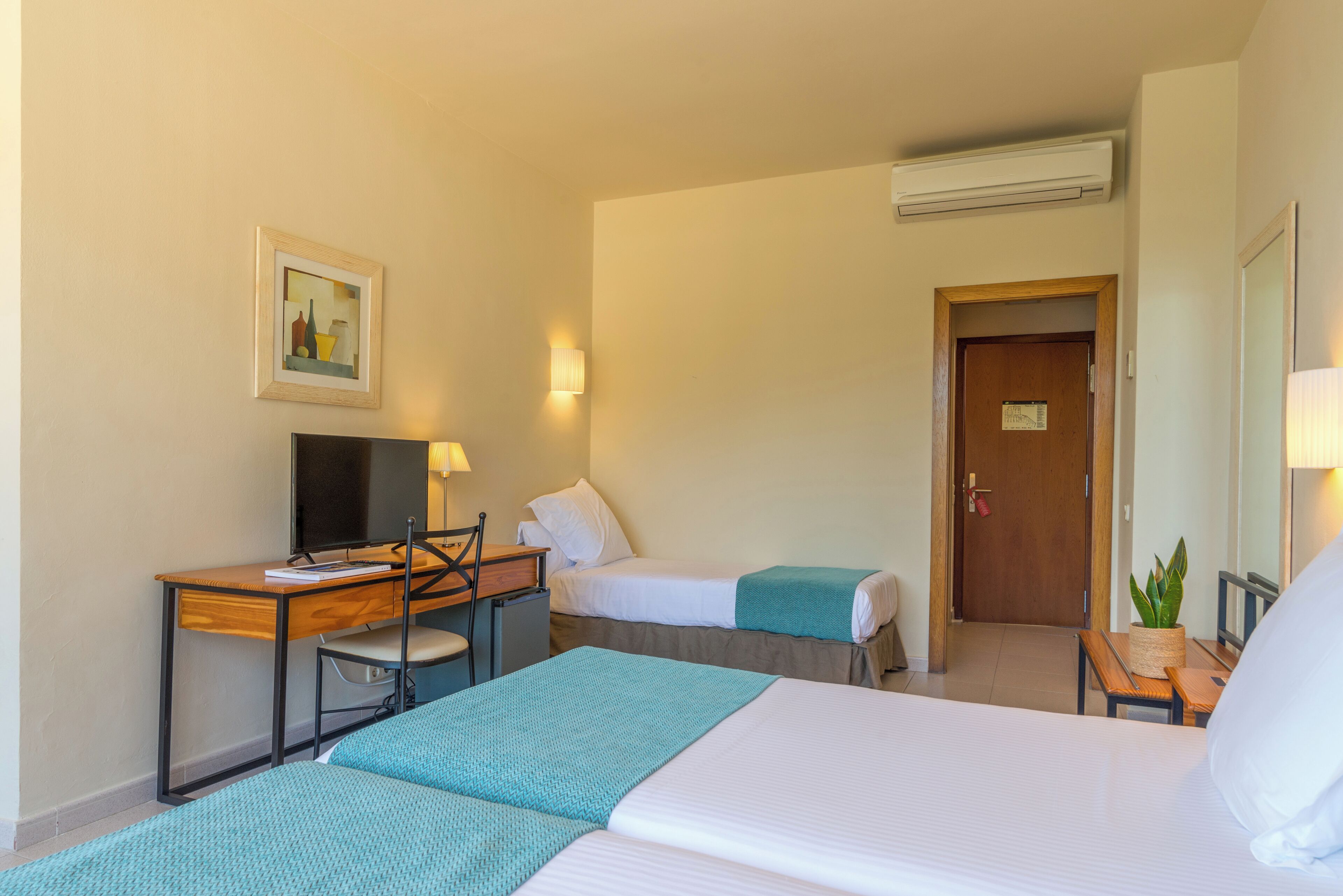 Une chambre d’hôtel avec un lit, un bureau et une chaise, une télévision et une porte.