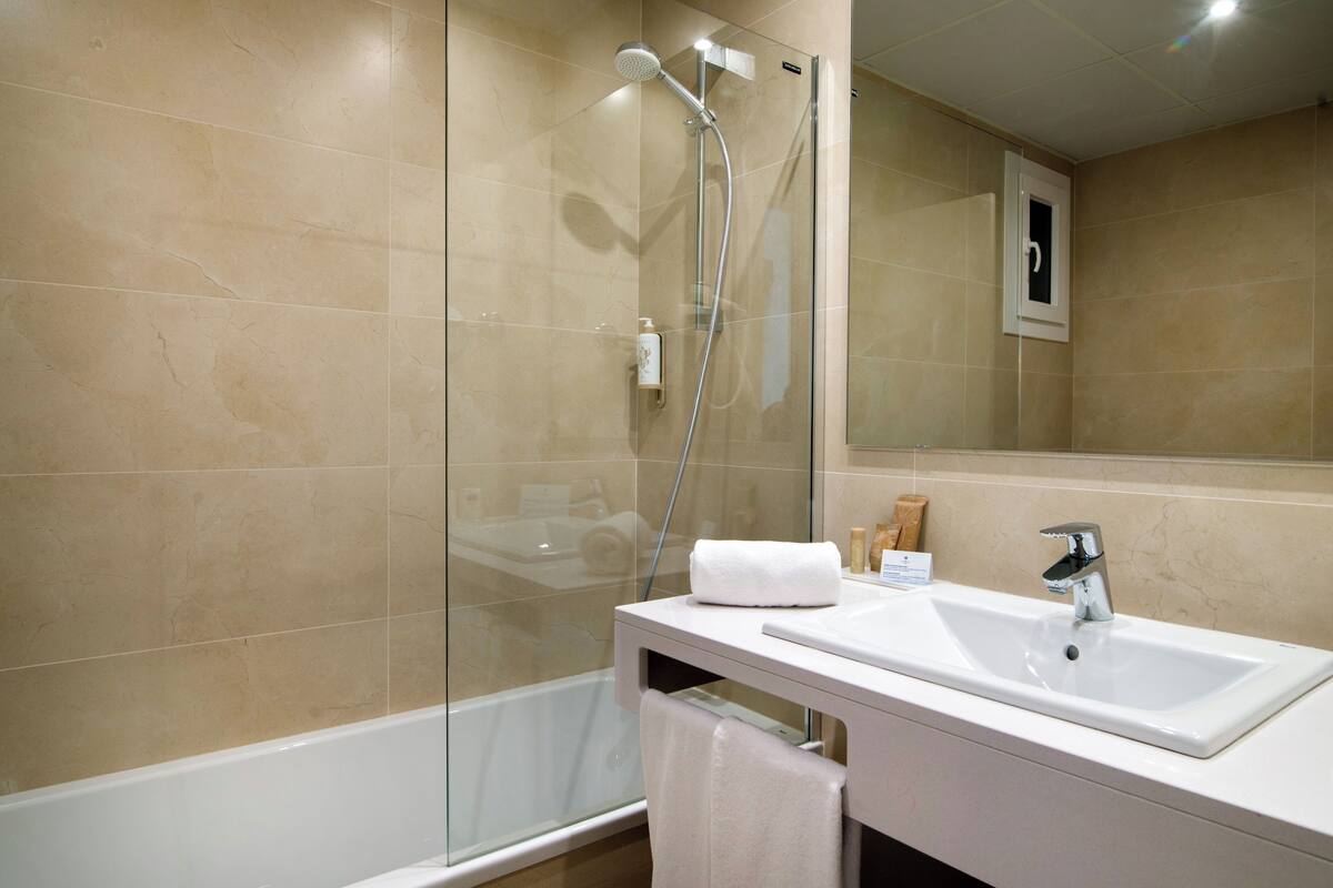 A modern bathroom with a glass-enclosed shower, a white sink, and a mirror.