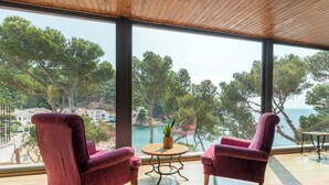 Una habitación con dos sillones cómodos orientados a un ventanal con vistas a una zona costera con árboles y una masa de agua.