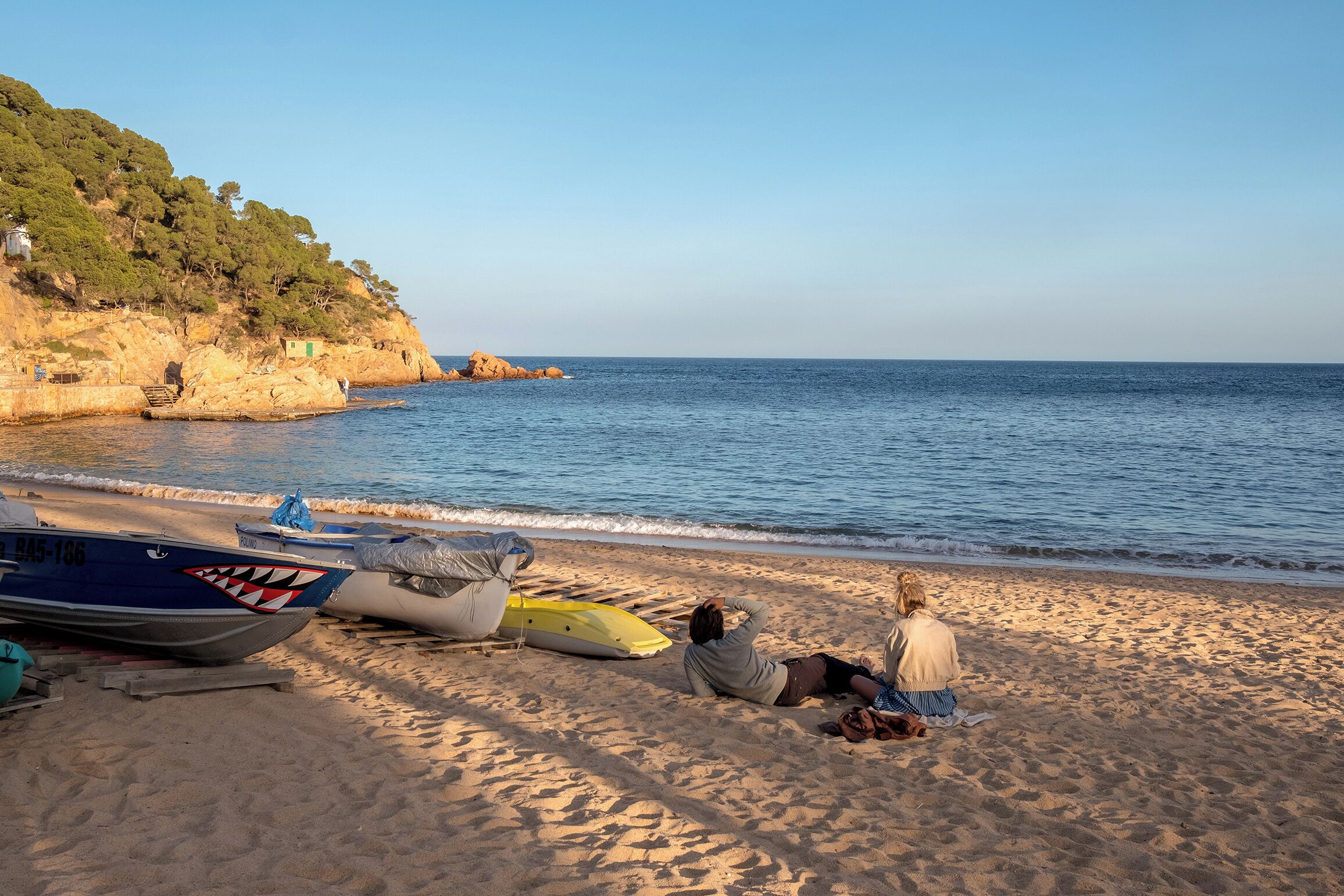 Une plage avec des bateaux et une personne assise sur le sable.