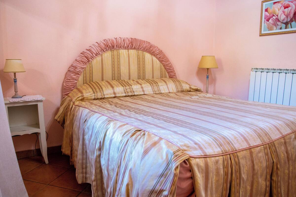 A bedroom with a bed, two bedside lamps, a white nightstand, and a radiator.