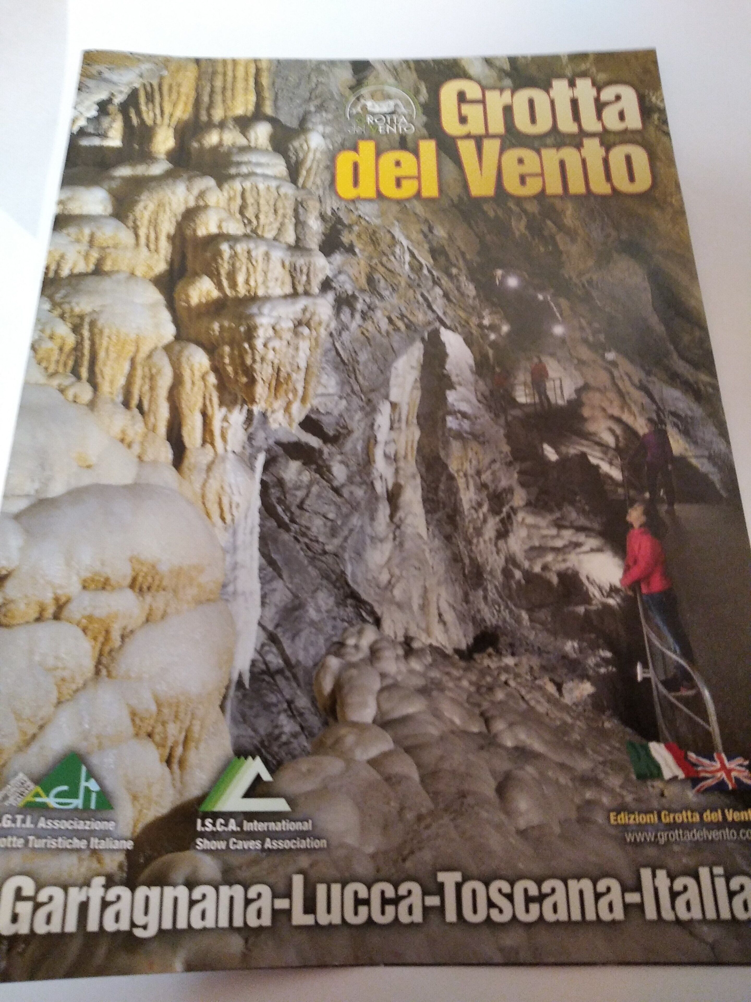 Eine Höhle mit Stalaktiten und Stalagmiten, eine Person beim Klettern, und ein Hinweis darauf, dass es sich um eine Touristenattraktion in Italien handelt.
