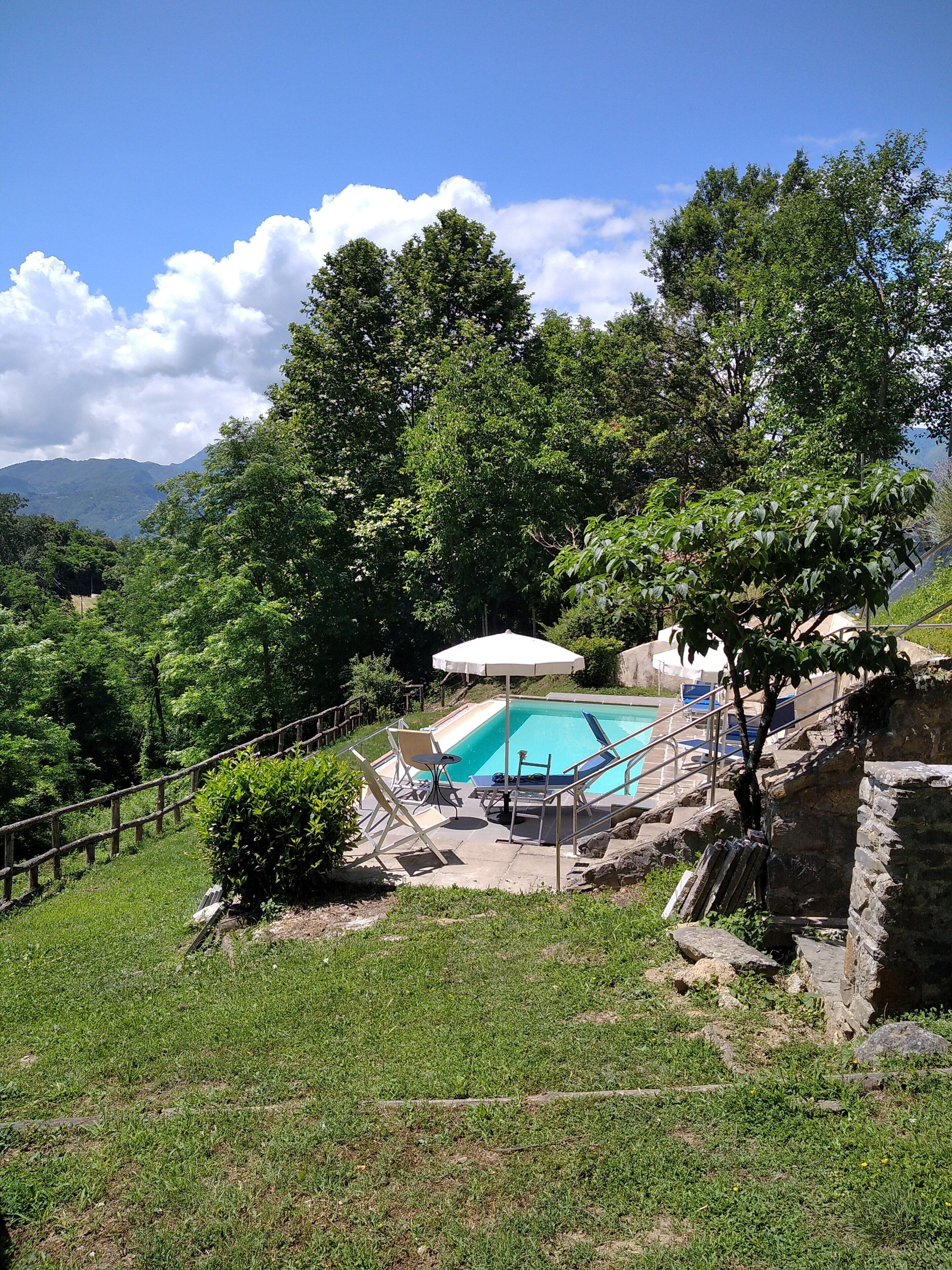 Un área de piscina con un muro de piedra, una valla de madera y vistas a montañas al fondo.