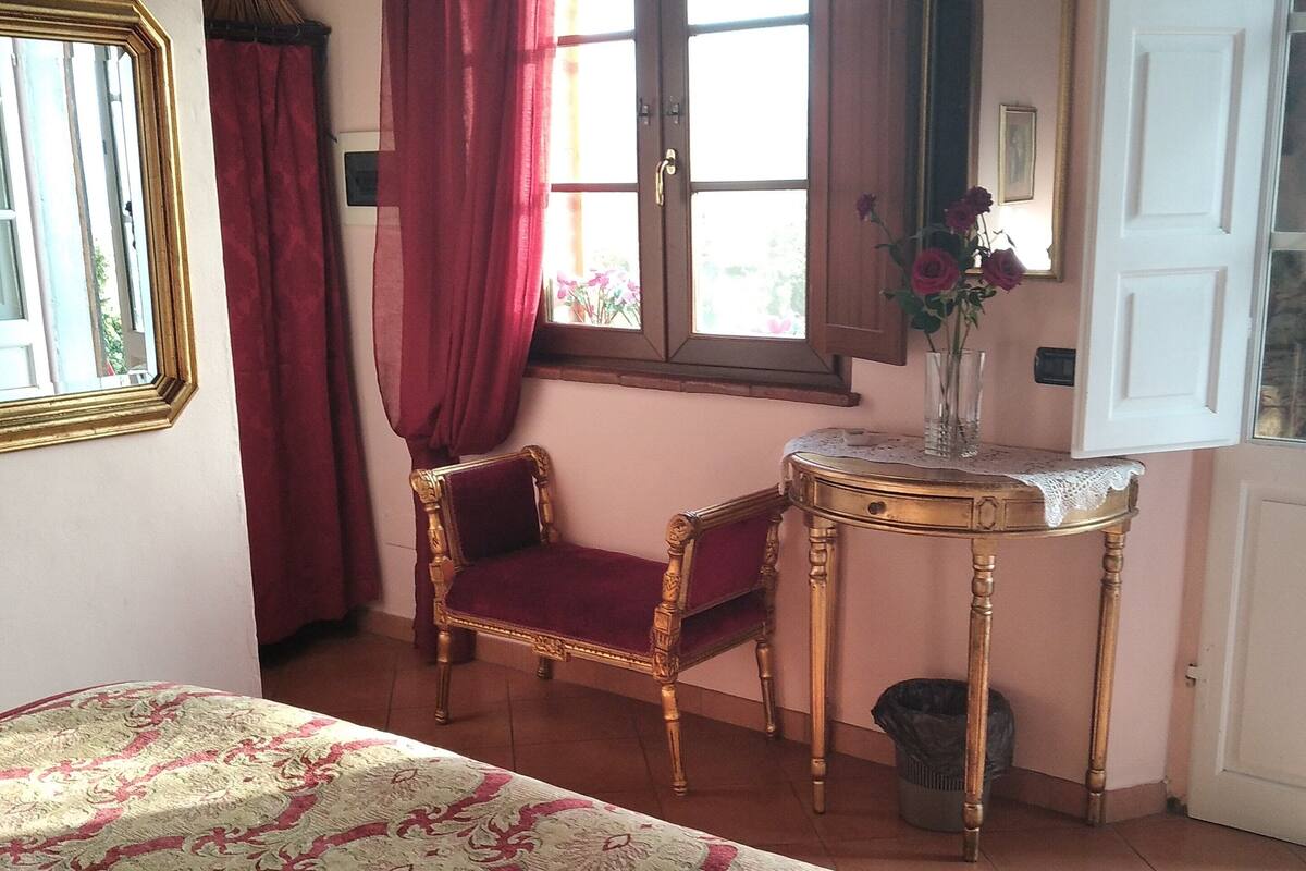 A room with a bed, a chair, a table with a vase of flowers, and a window with curtains.