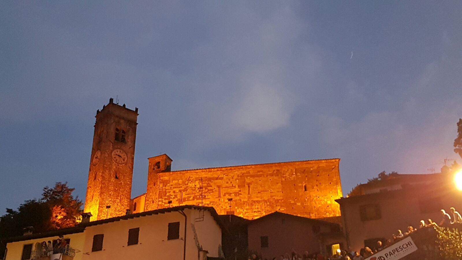 A historic building with a clock tower and a large illuminated wall at dusk.