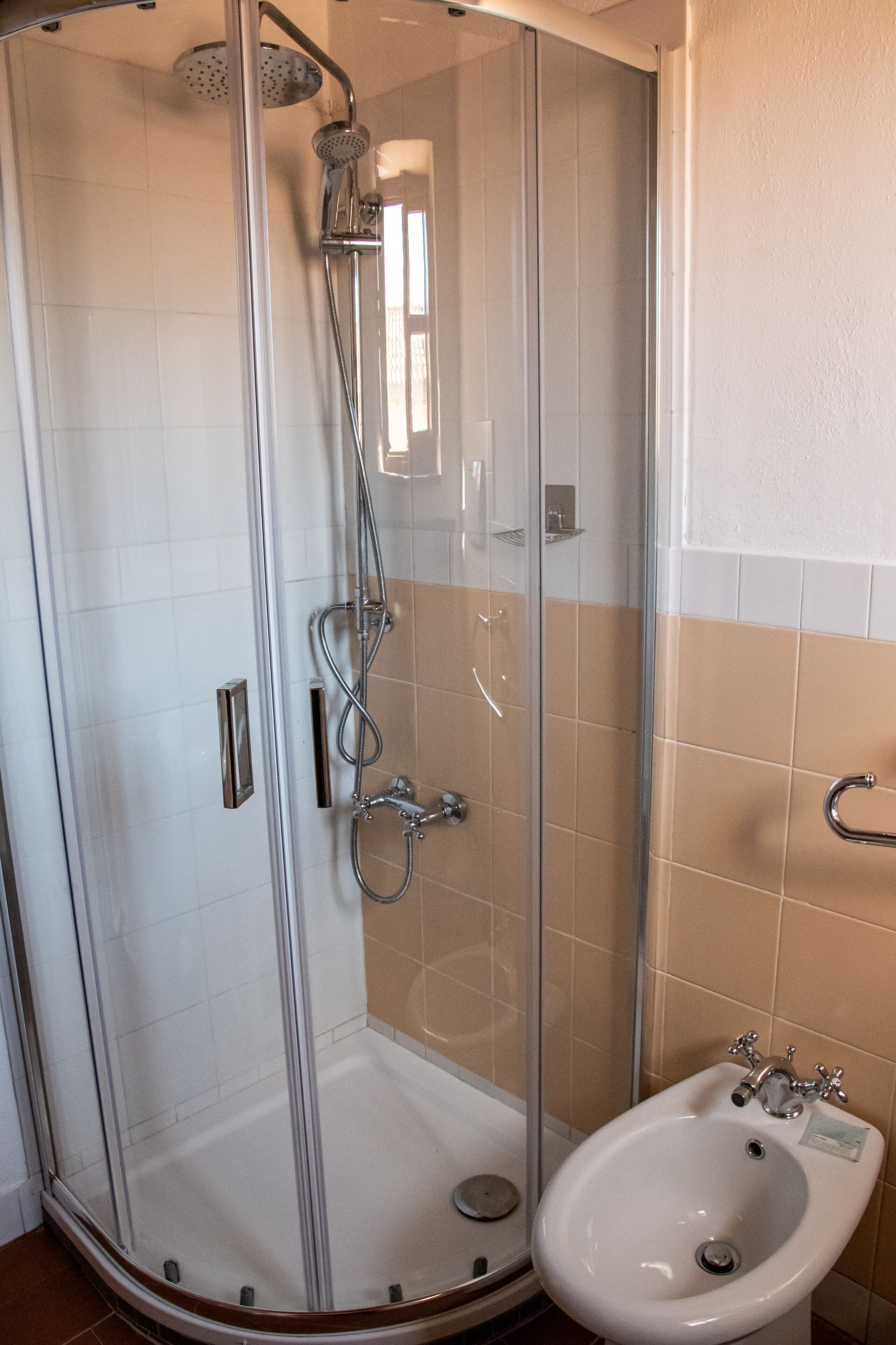 A glass-enclosed shower with a handheld showerhead and a wall-mounted faucet.