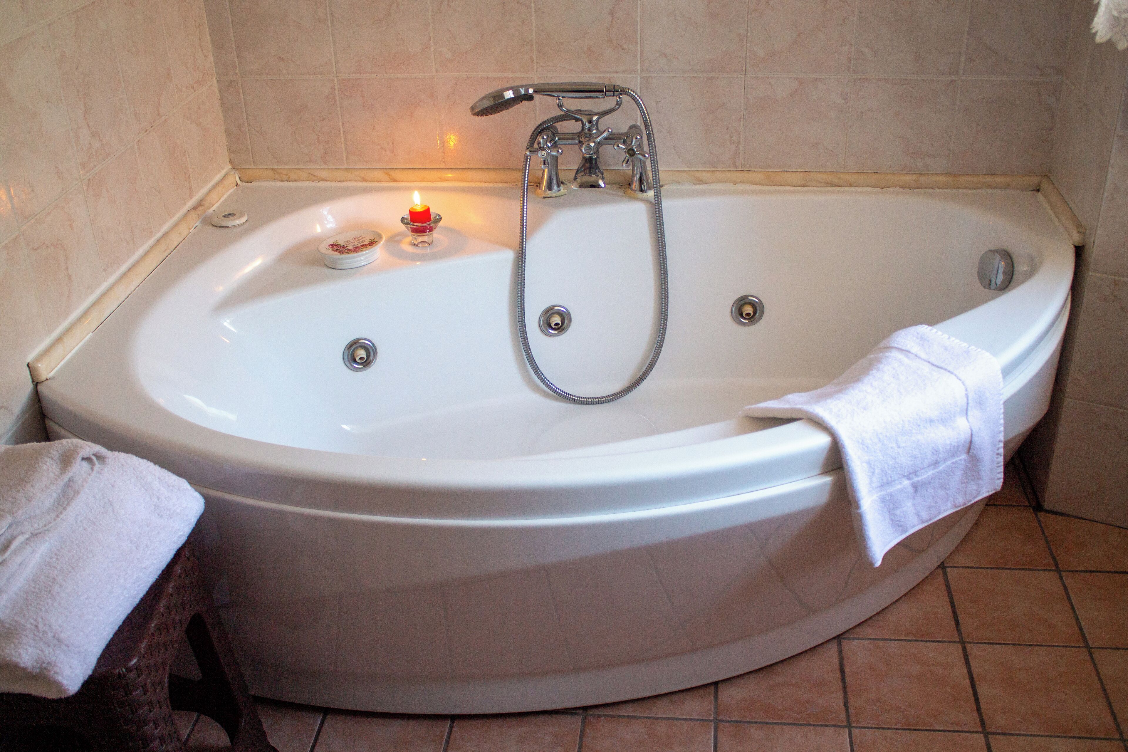 A large, white bathtub with a handheld showerhead and a small candle on the edge.