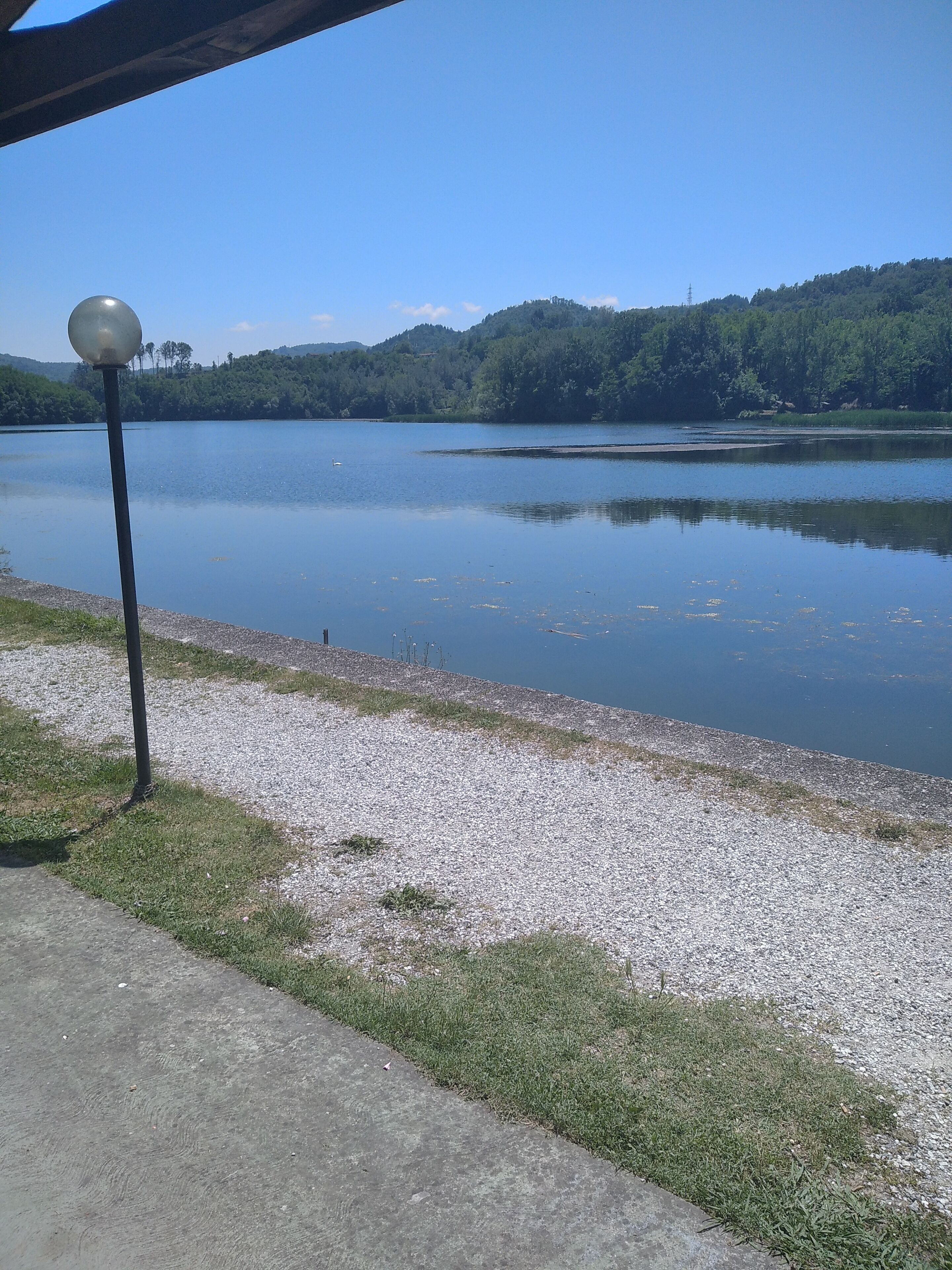 Vista tranquila de um lago, com um caminho de cascalho e um poste de luz.