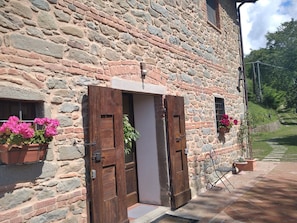 A stone building with a wooden door, potted plants, and a small outdoor seating area.