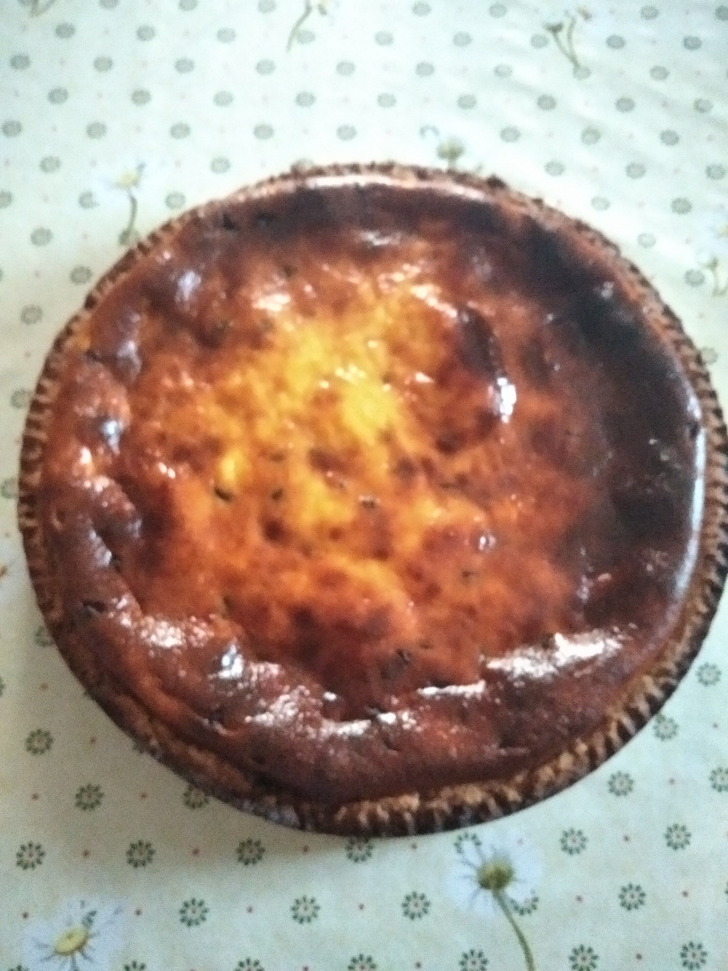 En rund, bakad rätt med en gyllenbrun yta, serverad på ett mönstrat bordsduks.